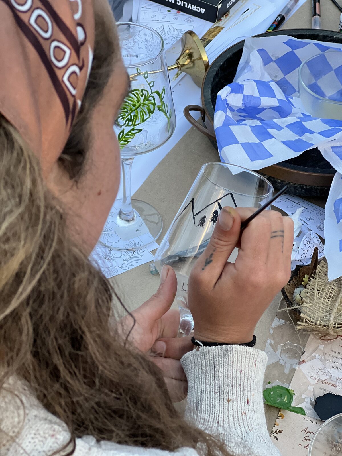 Mãos pintando montanhas e pinheiros em uma taça de vidro