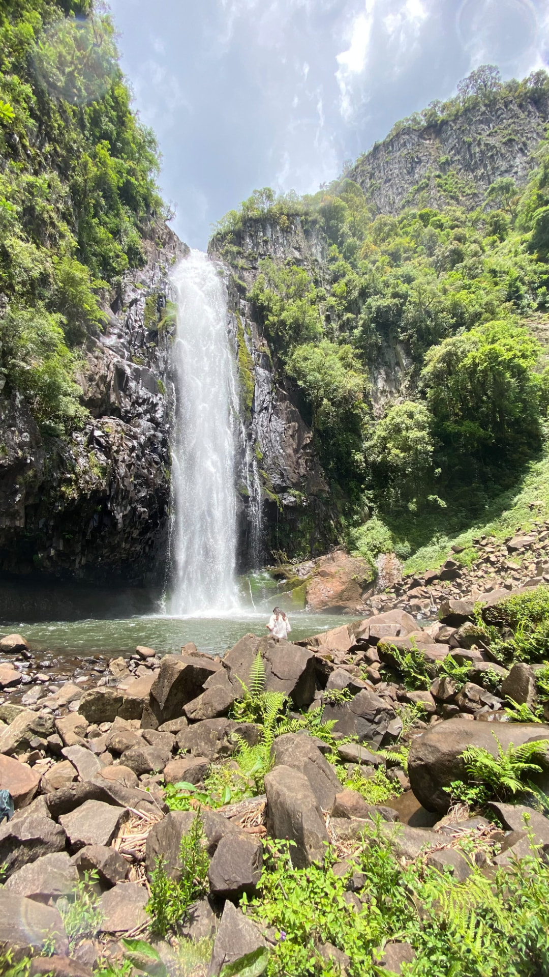 Cachoeira entre paredões de pedra e vegetação, com uma pessoa junto à água