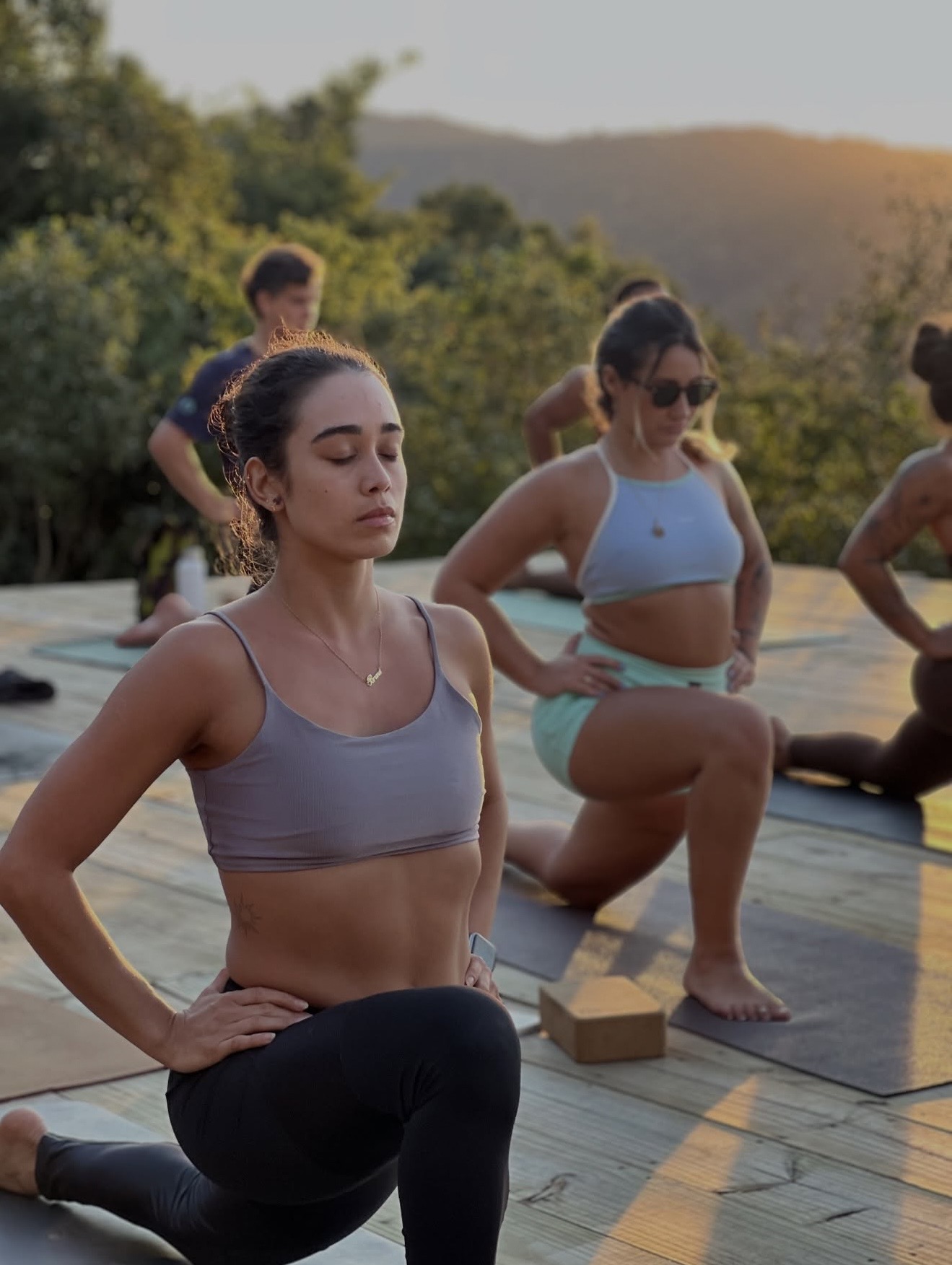 Mulheres praticando yoga no deck de madeira ao entardecer, com as montanhas ao fundo