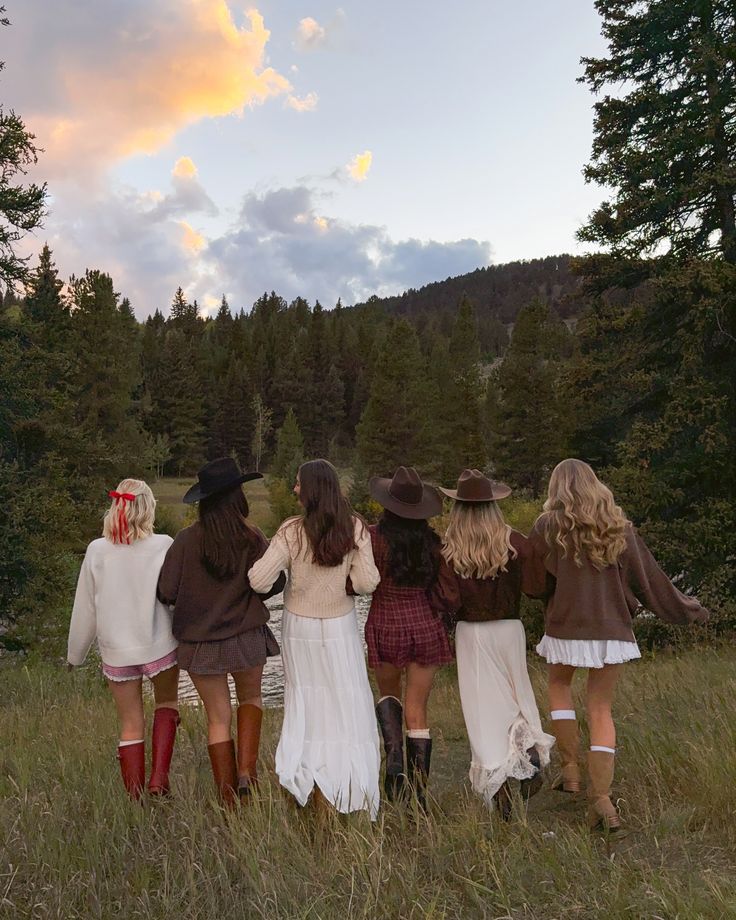 Seis mulheres caminhando juntas pelo campo, de frente para a mata ao entardecer